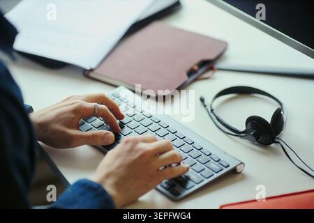 Close up of hands of young worker typing on keyboard at office desk, managing digital tasks and communication. Ideal for business productivity, remote work, workflow content Stock Photo