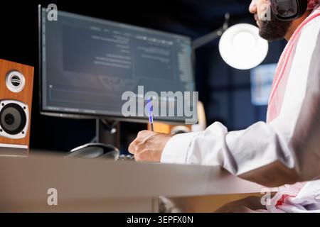 Middle Eastern software developer coding on a laptop to demonstrate the foundations of software development; while using wireless headphones, an Arab guy runs algorithms. Stock Photo