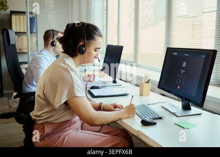 Young adult business team working in call center office, answering customer support requests and taking notes. Ideal for customer service, CRM, help desk, outsourcing marketing Stock Photo