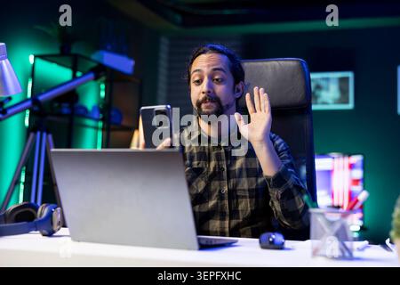 Young man making hello gesture on a conference call with family on his mobile device. Stock Photo