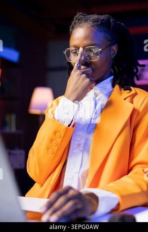 Focused freelancer working from home, adjusting eye glasses on nose, typing on laptop while remote employee in apartment scrolling on notebook and sending emails to business associates. Stock Photo