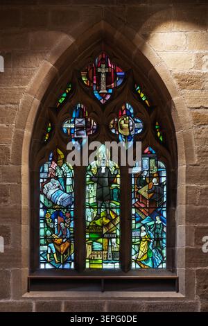 Detailed vertical view of the richly coloured Plague Window created by Alfred Fisher inside St Lawrence Church in Eyam, Derbyshire Stock Photo