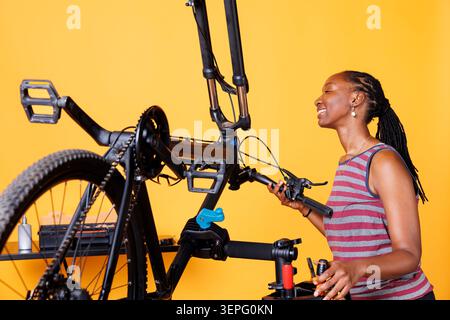 Athletic Black woman engrossed in fixing broken bike components with specialist tools while African American lady expertly adjusting, examining, and repairing bicycle parts for optimal performance. Stock Photo