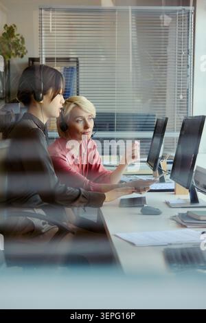 Vertical shot of Asian young adult woman and Caucasian middle aged woman working in call center, reviewing customer support data for training, service quality, team management Stock Photo