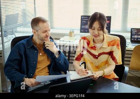 Young adult diverse coworkers reviewing documents and taking notes in office, collaborating on project planning and teamwork. For business strategy, corporate training, productivity marketing Stock Photo