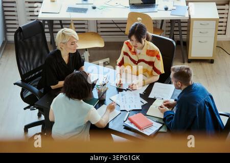 High angle view of diverse young adult team reviewing reports and discussing strategy in office, representing collaboration, brainstorming and planning. Ideal for business teamwork marketing Stock Photo