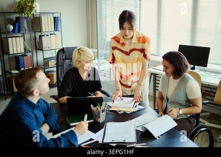 Diverse young team collaborating in disability inclusive office, reviewing documents and planning project strategy. Ideal for business teamwork, inclusive workplace, corporate communication marketing Stock Photo