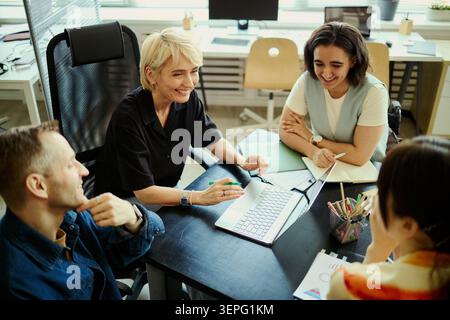 Diverse business team collaborating around laptop in office, discussing project strategy and sharing ideas. Ideal for workplace teamwork, leadership, planning, corporate communication Stock Photo