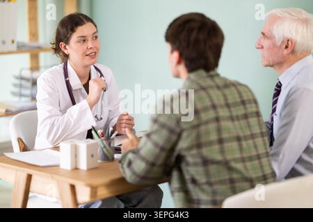 Senior man next to his adult son sits in the doctors office Stock Photo