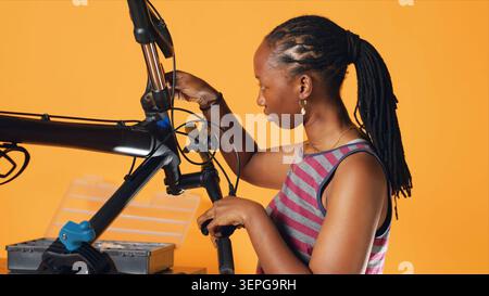 Engineer uses screwdriver to tighten brake levers screws on bicycle handlebars, examining components, studio background, expert unscrewing defective bike parts in order to recondition them, studio A. Stock Photo