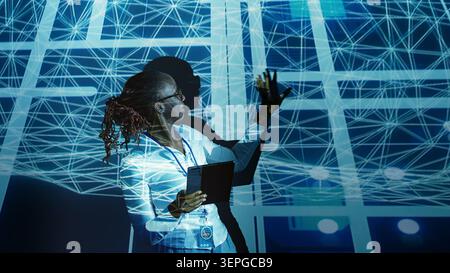 Computer scientist programming in AI server farm housing advanced equipment used for machine learning training, developer running code on tablet to upgrade artificial intelligence rigs. Stock Photo