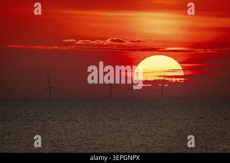 Dramatic sunset over the sea, wind turbines and wind turbines on the horizon, streaks of clouds, Houvig Beach, North Sea, Denmark Stock Photo