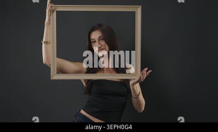 Woman holding an empty wooden frame around her face against a dark background Stock Photo
