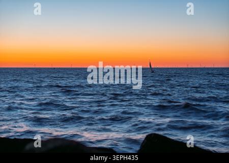 Sunset over the North Sea with wind farm and sailing boat off IJmuiden coast in the Netherlands Stock Photo