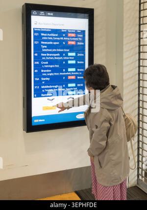 A woman using an interactive timetable display panel in Durham bus station, England, UK Stock Photo