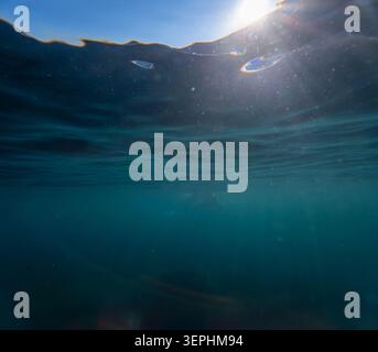Underwater sunlight ocean view looking up from below at the bright sun shining through ripples on the surface of deep blue sea Stock Photo