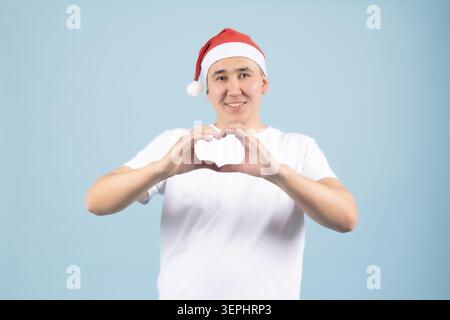 Man wearing a santa hat making a heart gesture with both hands posing Stock Photo