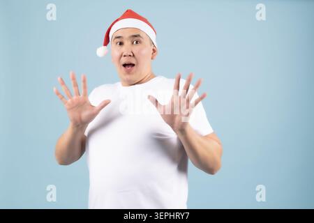 Surprised man wearing a santa hat spreading hands in shock or Stock Photo