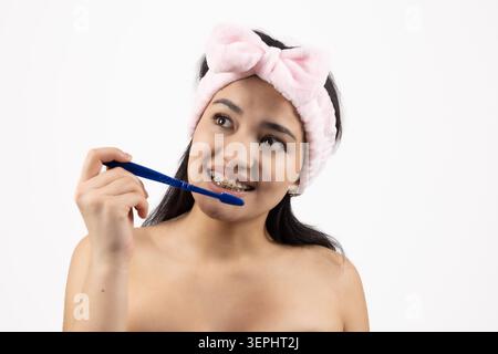 Young woman brush teeth holding toothbrush looking up thoughtfully Stock Photo