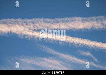 White contrails and wispy clouds forming parallel lines across a clear blue sky. Stock Photo