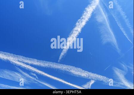 Deep blue sky with crisscrossing white contrails and diffused cirrus cloud formations. Stock Photo