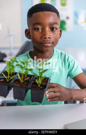 African American child in mint-tee holding black tray with six plants at school by renewable models Stock Photo