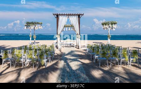 Elegant beach wedding ceremony setup on a sandy tropical shore in Bali, Indonesia, with white floral decorations, chairs, and a romantic ocean backdro Stock Photo