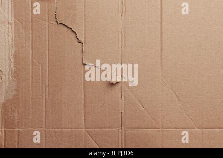 Abstract closeup of old torn reused cardboard sheet with weathered fibers. Folded paper edges and worn cracks. Sustainable packaging material Stock Photo