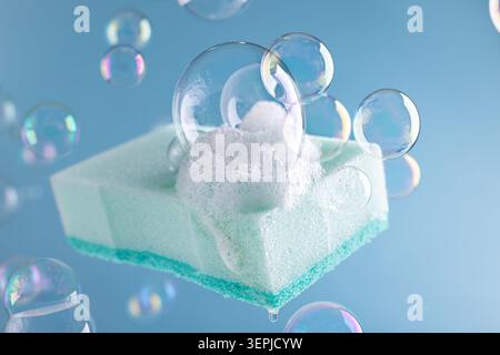 Floating light blue cleaning sponge with soap foam and many bubbles on fresh blue background. Housework or cleaning services of home. Cleaning supplie Stock Photo