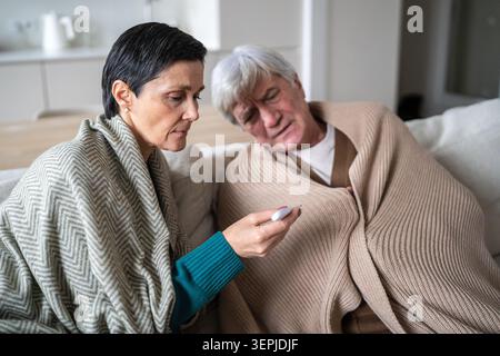 Tired unwell senior man woman on sofa under plaids, flu infection quarantine at home Stock Photo