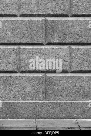 A close-up vertical view of a gray, speckled granite block wall with beveled joints, black and white background photo Stock Photo