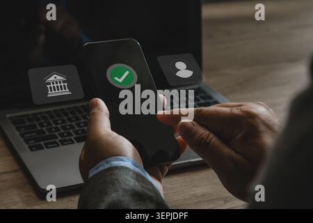 Person using smartphone beside laptop with digital banking verification interface for online account deposit, secure mobile payment, internet banking, Stock Photo
