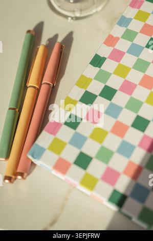 Colorful modern pens next to a checkered notebook in sunlight Stock Photo