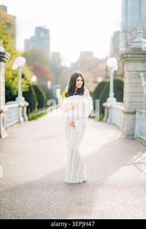 Pregnant woman embracing belly on sunny street outdoors Stock Photo