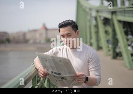 Young Asian man reading newspaper on a city bridge Stock Photo