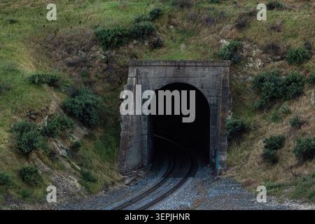 Train tracks lead into a dark mountain tunnel Stock Photo