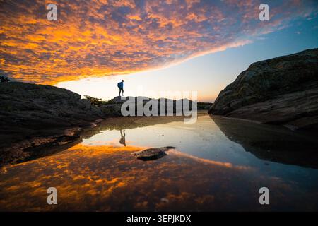 Hiker standing on rocks watching a dramatic sunset Stock Photo