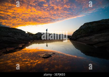 Hiker silhouetted on rocks watching fiery sunset Stock Photo