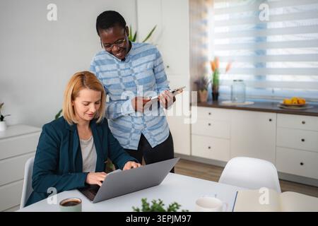 Diverse women collaborating on laptop and holding tablet at home Stock Photo