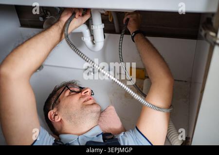 Plumber working on a sink pipe blockage in kitchen Stock Photo
