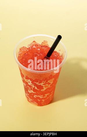 Red fruit slushie drink in plastic cup on yellow background Stock Photo