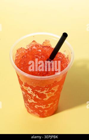 Red fruit slushie drink in plastic cup on yellow background Stock Photo