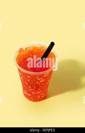 Red fruit slushie drink in plastic cup on yellow background Stock Photo