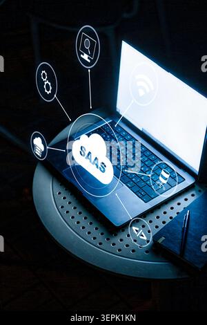 Saas symbols and concepts around an open laptop on a table during late evening hours Stock Photo