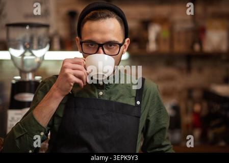 A close up of a barista drinking a hot beverage from a white cup Stock Photo