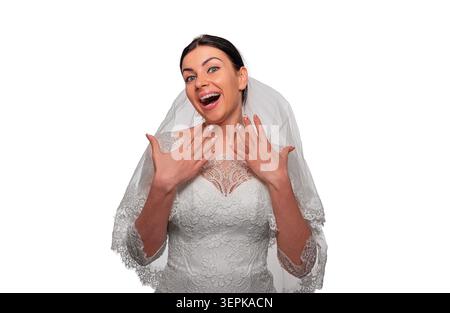 An excited and cheerful bride poses in her white wedding dress and veil while showing off her manicure. Stock Photo