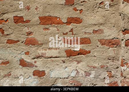 Full frame textured shot of an old decaying brick wall with crumbling tan plaster exposing red clay bricks Stock Photo