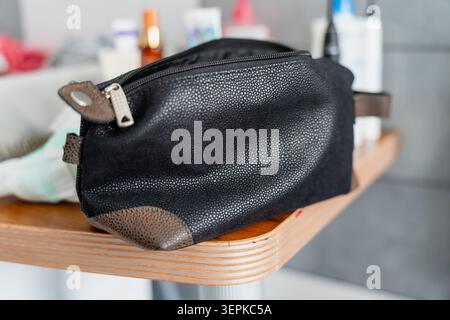 Men cosmetic pouch for hygiene accessories resting on a wooden tabletop with blurred bathroom essentials, personal care and morning routine Stock Photo