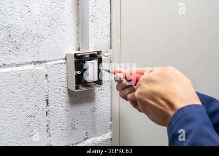 Electrician mounting electric sockets on the white wall. Electrician wiring a new build. Worker installing socket in new house. Man installing light s Stock Photo