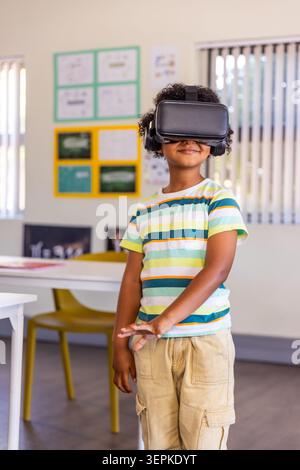 African American boy standing by table with yellow chair wearing VR headset headphones Stock Photo
